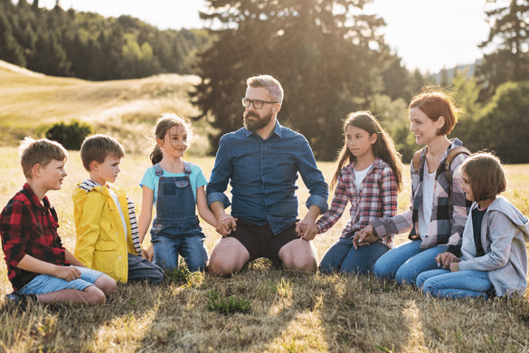 a group of kids on a field trip sit in a field
